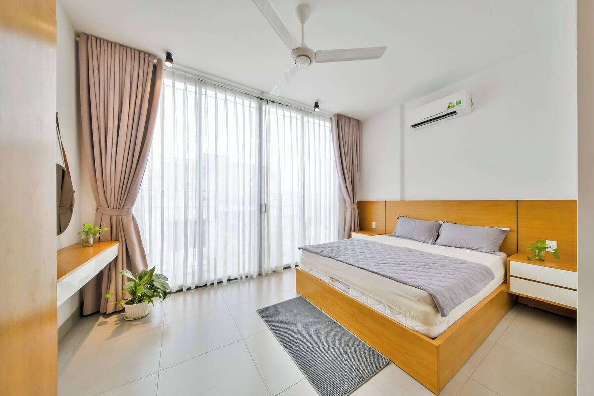 A modern bedroom with a bed, bedside tables, a ceiling fan, and a large window with curtains.