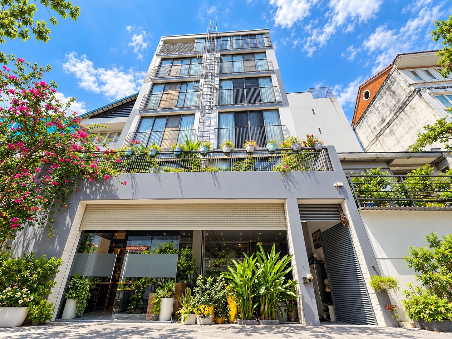 A modern building with a glass facade, a visible fire escape, and potted plants on the balconies.