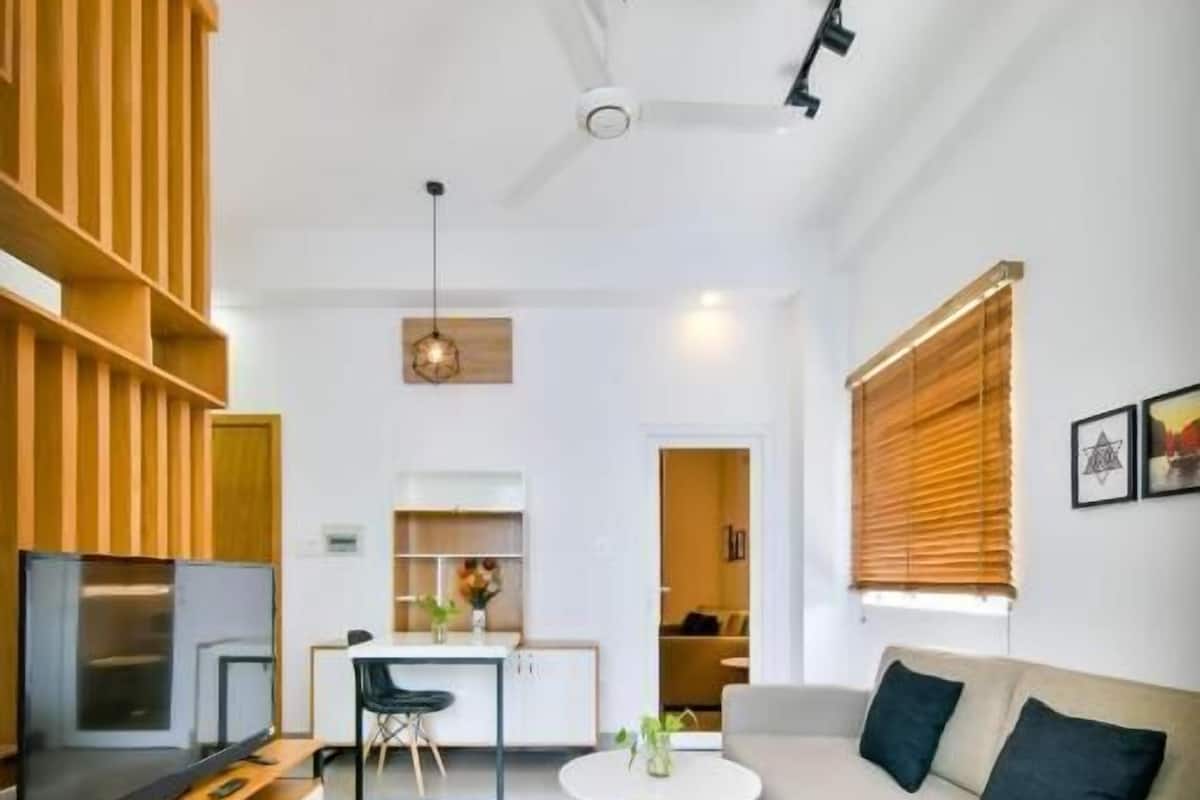 A modern living room with a sofa, TV, wooden shelving, and a dining area.