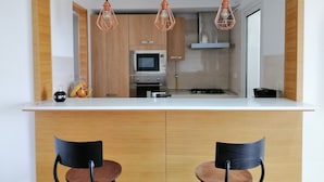 Une cuisine moderne avec des armoires en bois, un four à micro-ondes, une cuisinière à gaz et des luminaires suspendus. Il y a deux chaises au comptoir.