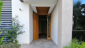 Une entrée moderne avec une porte en bois, un chemin pavé et de la verdure de chaque côté.