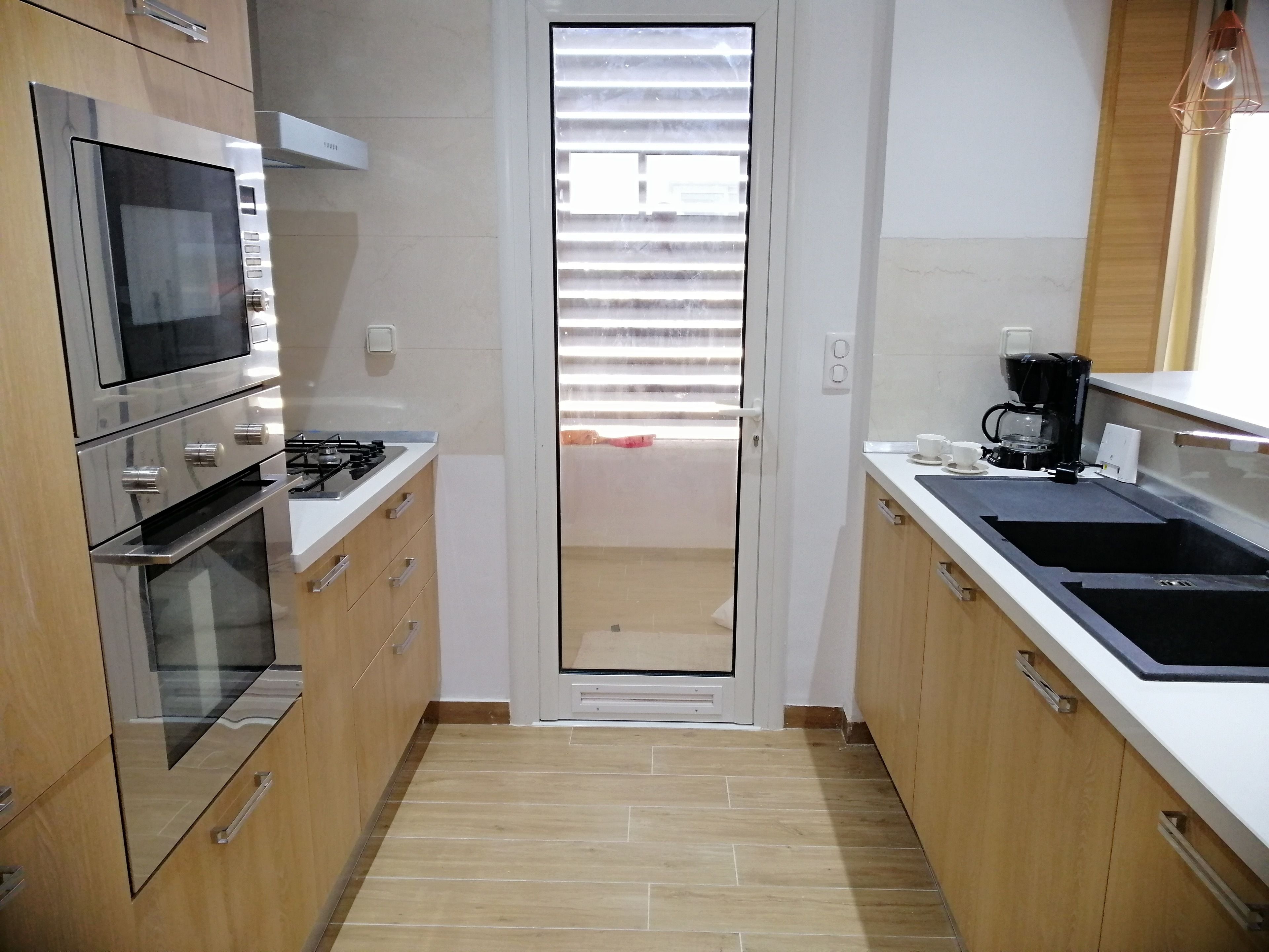 Een moderne keuken met roestvrijstalen apparatuur, houten kastjes, een zwart aanrecht en een raam met jaloezieën.