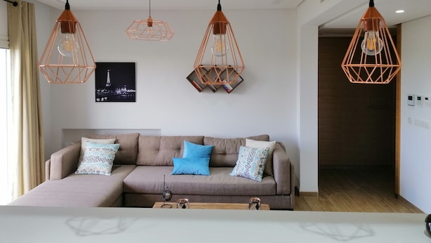 Un salon moderne avec un canapé d’angle, des luminaires suspendus et un tableau encadré au mur.