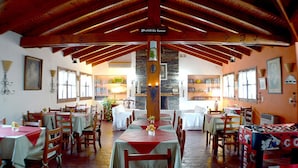 A restaurant with wooden beams, tables with red tablecloths, and a stone pillar. - Posada San Bras (Villa General Belgrano)