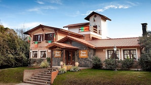 A two-story building with a stone facade, a red-tiled roof, and a small tower. There are signs with the name 'San Bras' on the front. - Posada San Bras (Villa General Belgrano)