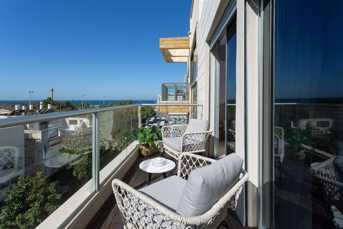 Ein Balkon mit Korbmöbeln, einer Glasreling und Blick aufs Meer.