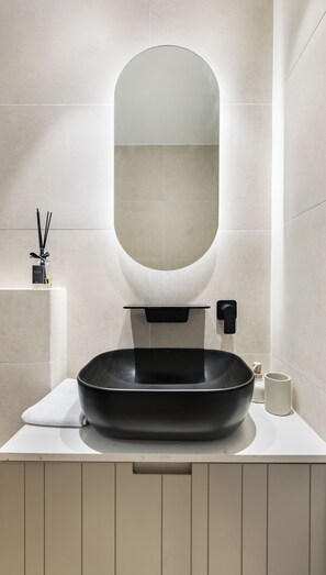 A modern bathroom with a large oval mirror, a black sink, and a white countertop. - Mr. Yavos - By TLV2GO (Tel Aviv)