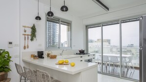 A modern kitchen with a central island, bar stools, a large window, and a balcony with outdoor seating. - Mr. Yavos - By TLV2GO (Tel Aviv)