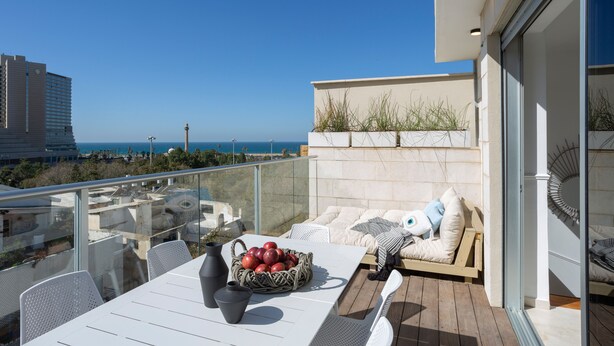 A balcony with a table, chairs, and a basket of apples. There is a view of the sea and buildings in the background. - Mr. Yavos - By TLV2GO (Tel Aviv)