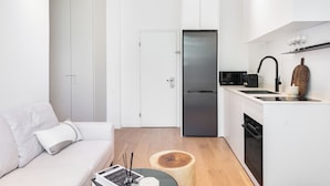 A modern kitchen with a refrigerator, microwave, and sink. There is a wooden cutting board and a small table with a book and candle. - Mr. Yavos - By TLV2GO (Tel Aviv)