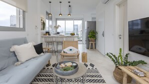 A modern living room with a sofa, coffee table, and a dining area with chairs and a kitchen in the background. - Mr. Yavos - By TLV2GO (Tel Aviv)