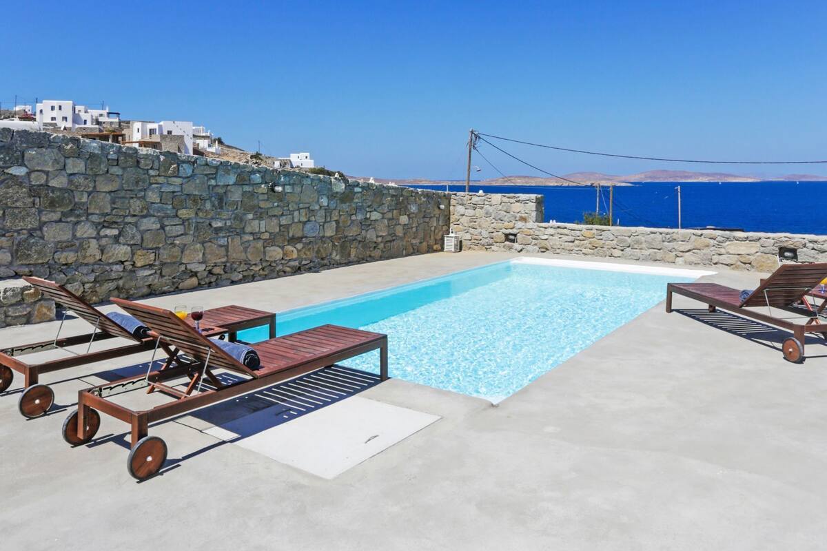A pool area with lounge chairs and a view of the sea.