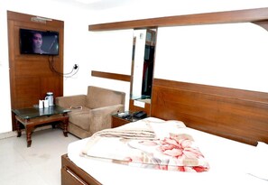 A hotel room with a bed, a chair, a small table, a television, and a mirror.
