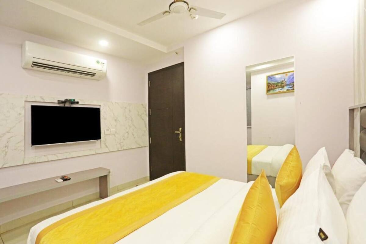 A hotel room with a bed, a TV, an air conditioner, and a door.