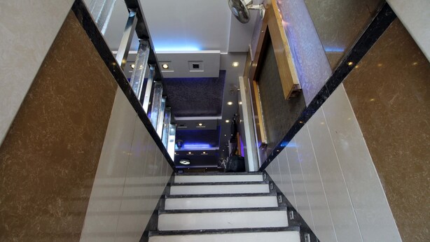 Blick auf eine Treppe in einem Gebäude mit modernem Design, mit einer Kombination aus Marmor- und Fliesenböden sowie einer Decke mit eingelassener Beleuchtung.