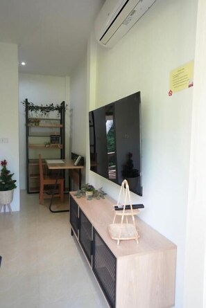 A modern living room with a flat-screen TV mounted on the wall, a wooden console table, and a seating area with a chair and a small table. - Tara Resort Samui (Koh Samui)