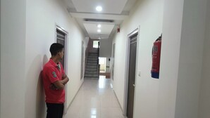 A hallway with a person standing, doors on both sides, a fire extinguisher, and a staircase in the distance. - Hotel Grace at Karol Bagh (New Delhi)