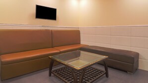 A waiting area with a brown leather sofa, a glass-top table, and a flat-screen TV mounted on the wall. - Hotel Grace at Karol Bagh (New Delhi)