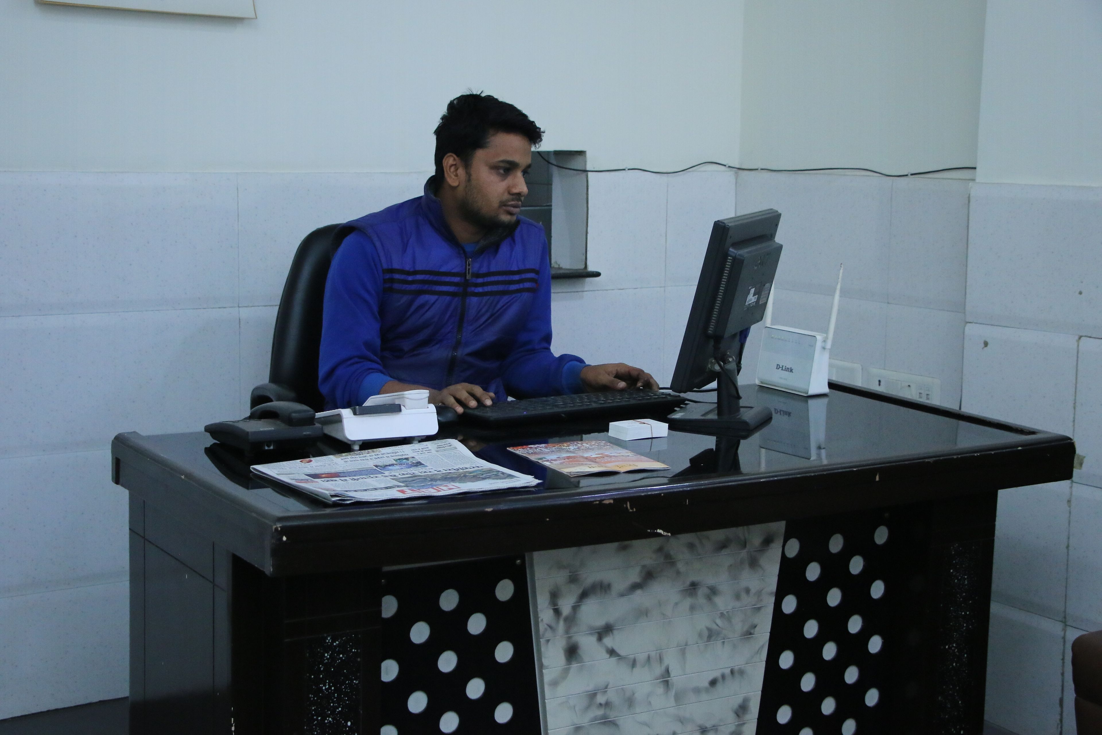 A person sitting at a desk with a computer, a phone, and some papers.