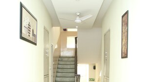A hallway with a staircase, exit sign, and lockers. - Hotel Grace at Karol Bagh (New Delhi)