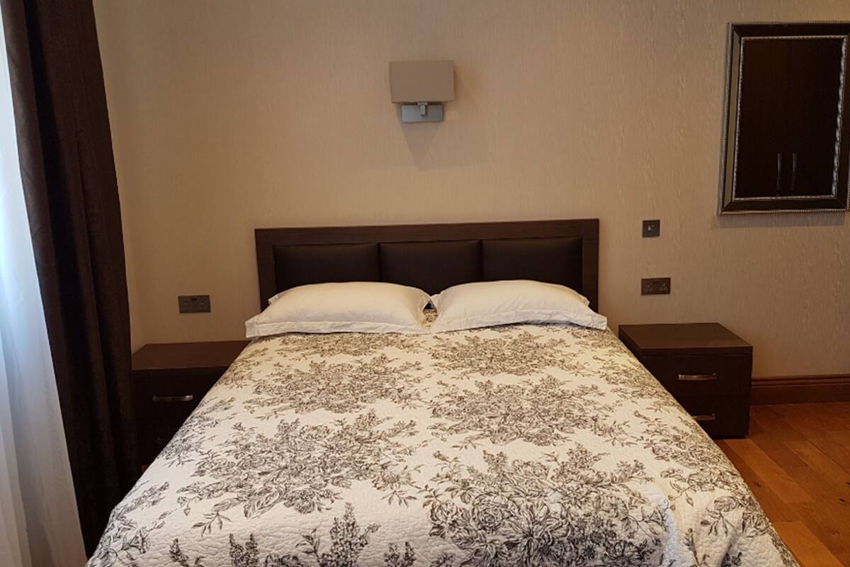 A bedroom with a large bed, two bedside tables, a wall-mounted light, and a door.