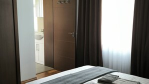 Hotellihuone, jossa on sänky, vaatekaappi, avoimesta ovesta näkyvä kylpyhuone ja ikkuna, jossa on verhot.