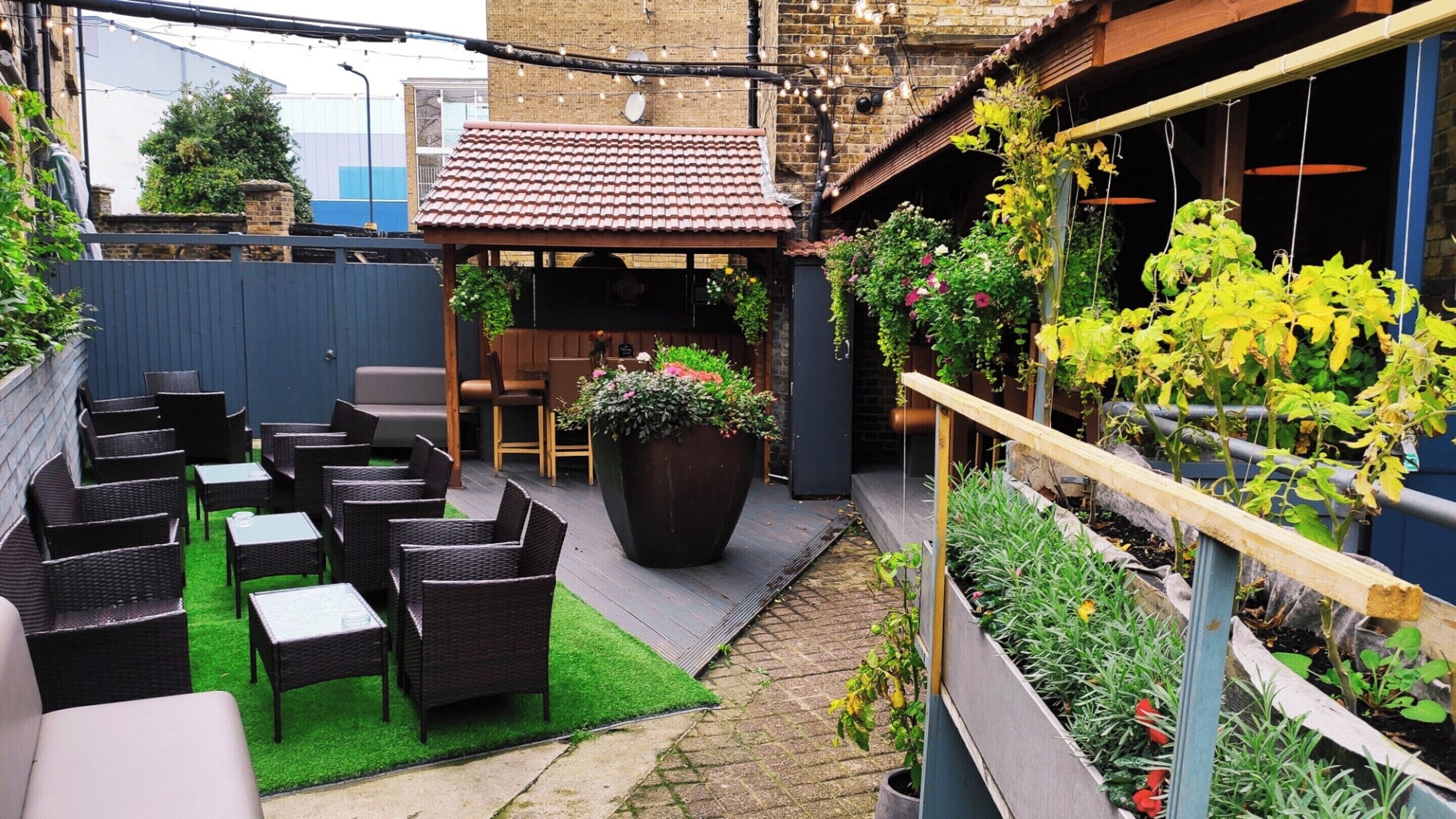 A patio with wicker furniture, a large planter with flowers, and a garden bed with plants.