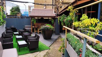 A patio with wicker furniture, a large planter with flowers, and a garden bed with plants.