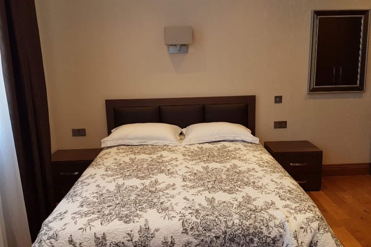 A bedroom with a large bed, two bedside tables, a wall-mounted light, and a door.