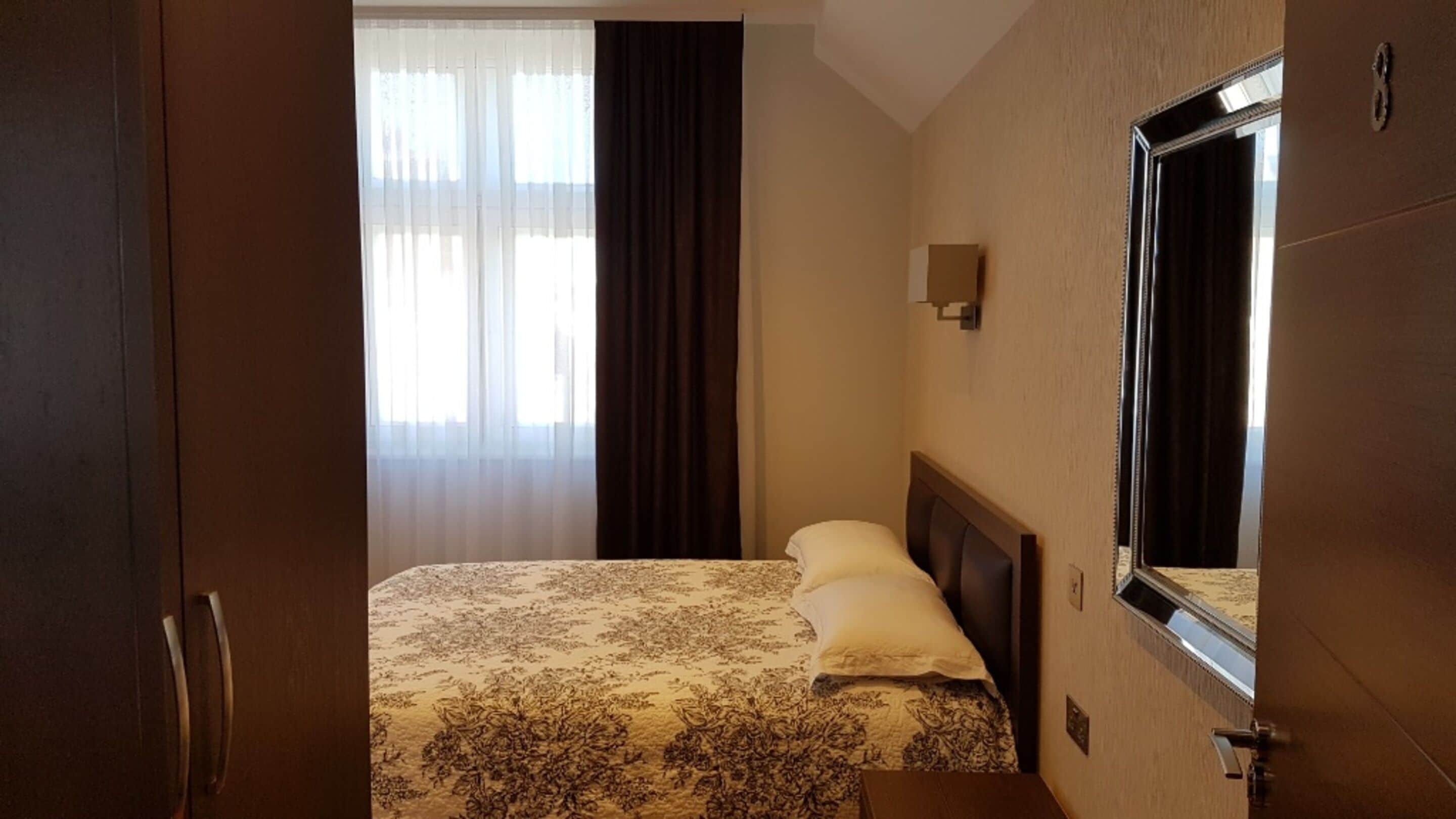 A hotel room with a bed, a nightstand, a mirror, and a window with curtains.
