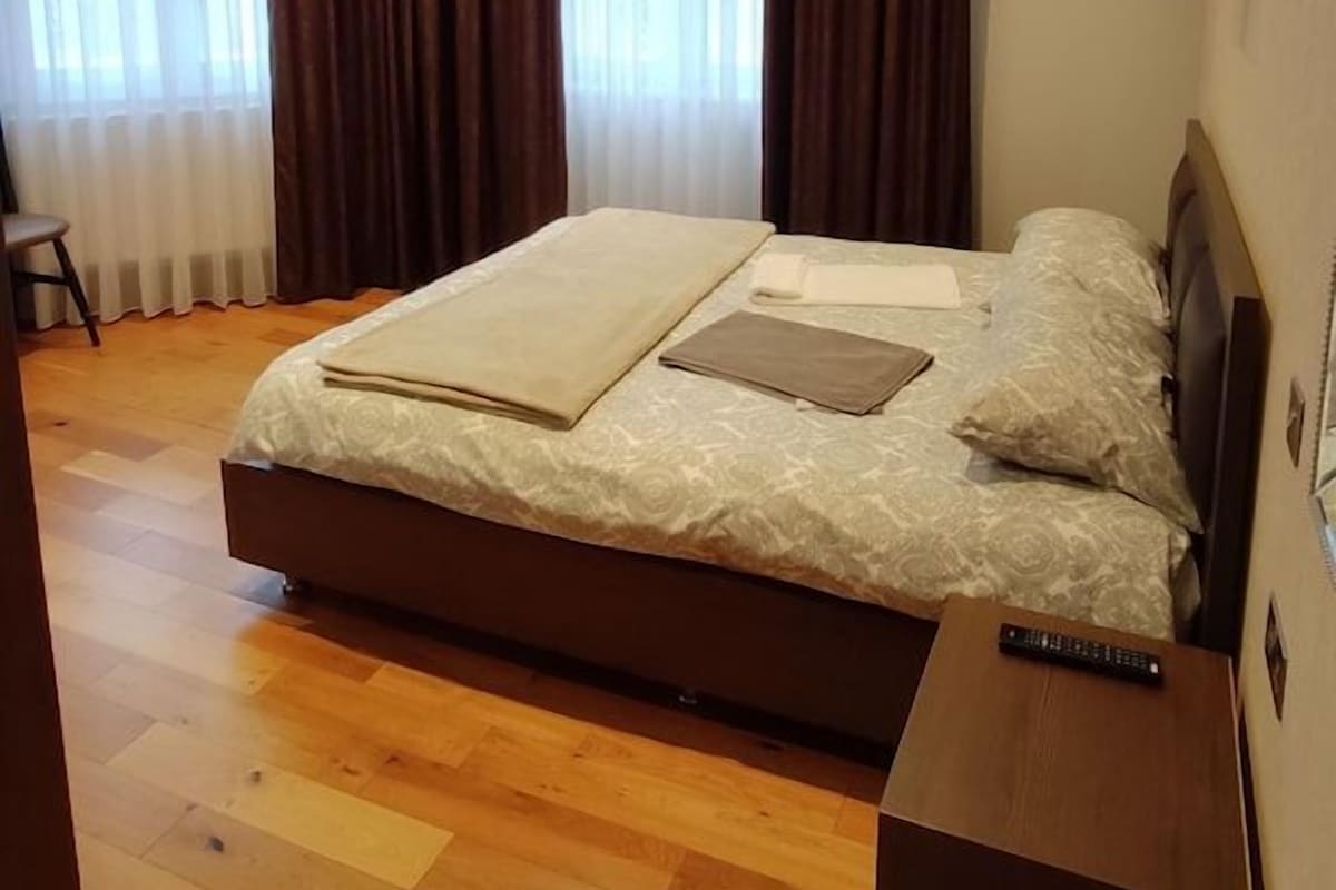 A bedroom with a bed, a nightstand, a remote control, and a chair.