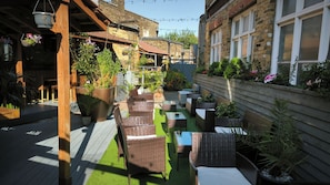 A patio area with wicker furniture, potted plants, and a wooden deck. - OYO The Kilburn Arms (London)