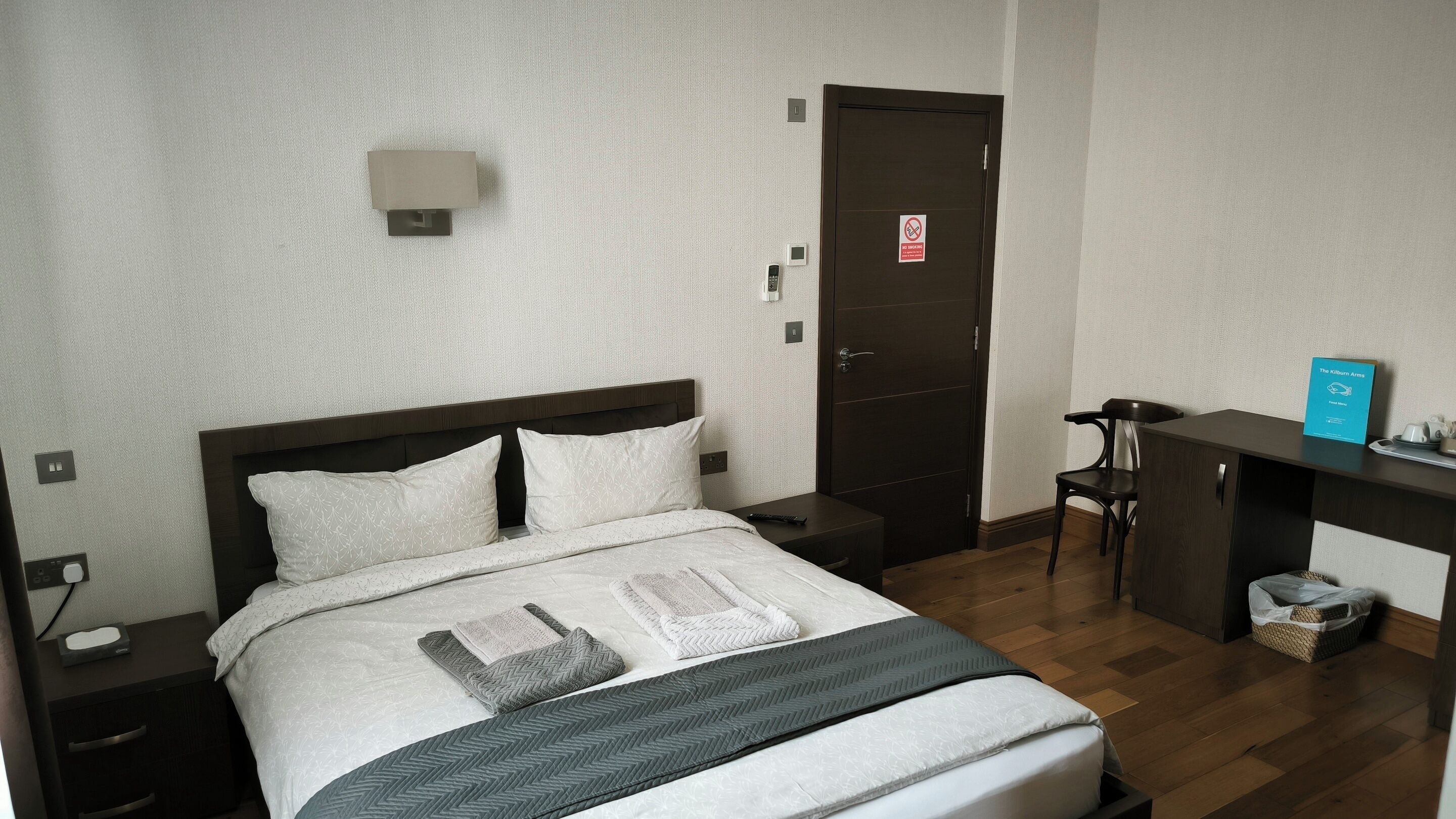 Une chambre d’hôtel bien rangée, avec un lit, une table de chevet et un bureau avec une chaise.