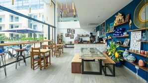 A modern cafe with wooden furniture, a glass display case, and decorative items on shelves. - Embassy Gardens Premier Suites (Accra)