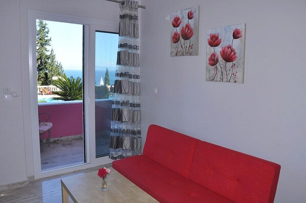 Un sofá rojo en una habitación con un ventanal corredero que da a un balcón con vistas al mar.