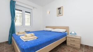 A bedroom with a bed, a nightstand, a lamp, a window with curtains, and a wall-mounted light fixture.