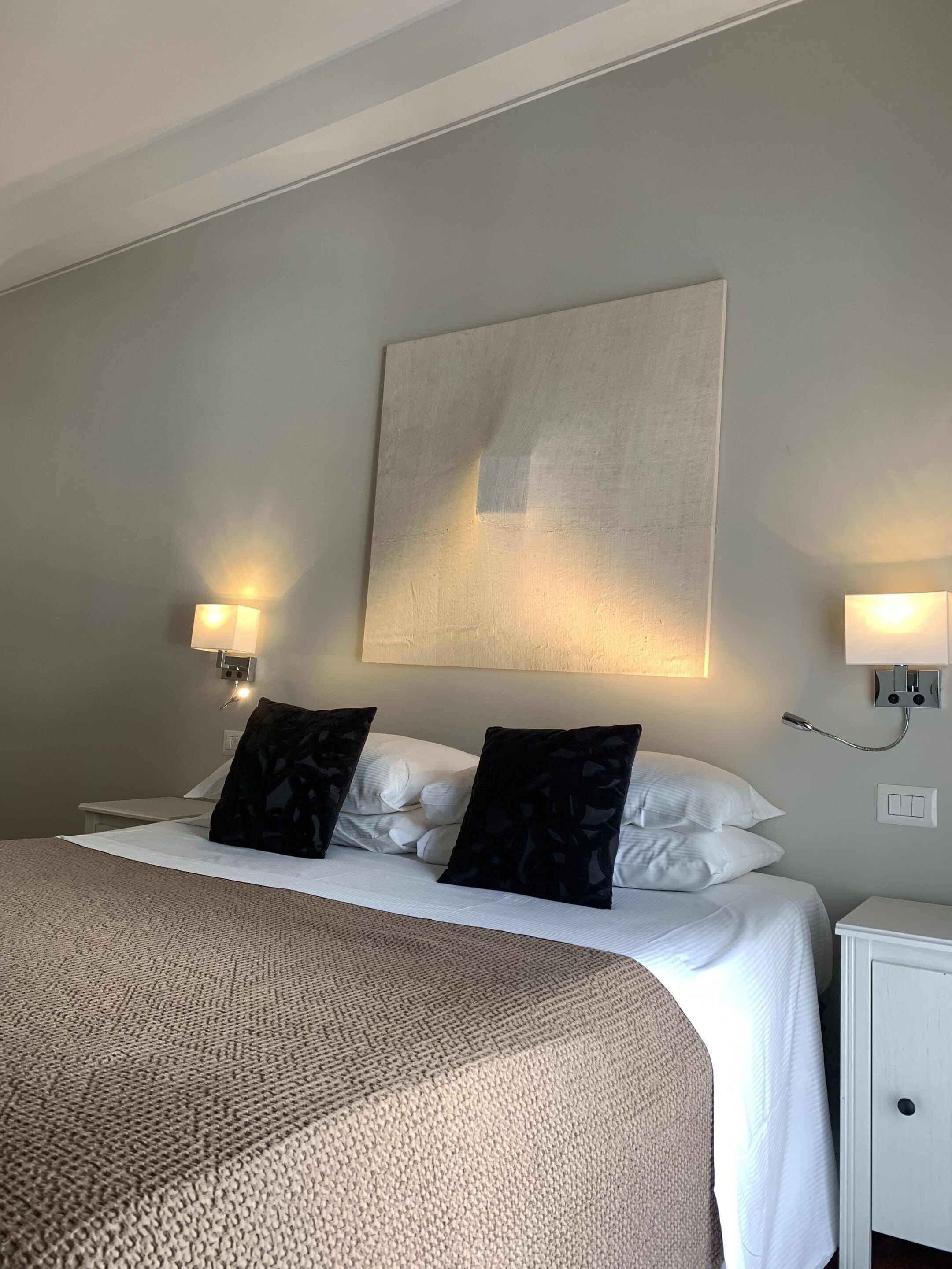 A hotel room with a bed, two bedside lamps, a nightstand, and a wall-mounted light fixture.