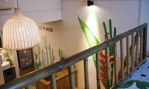 A staircase with a wooden railing, a hanging light fixture, and a wall with a cactus mural.