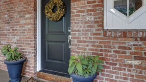 A brick house with a dark front door, a wreath, and two potted plants.