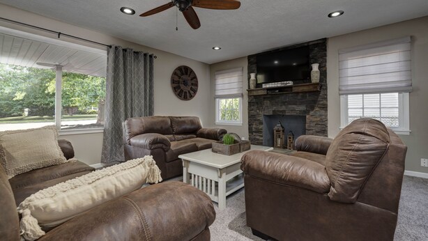A living room with leather sofas, a coffee table, a fireplace, and a ceiling fan.