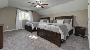 A bedroom with two beds, a ceiling fan, a window with curtains, and a nightstand.