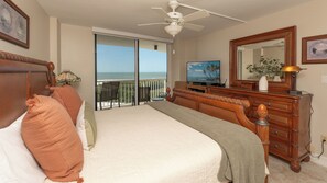 Quarto com cama, cômoda, televisão e varanda vista para o oceano.