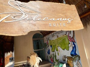A wooden sign with the text "DeCanus SUITE" and a mural with tropical wildlife. - Hotel Pelecanus Suites (Isla Holbox)