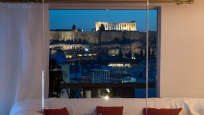 A modern hotel room with a large window offering a view of ancient ruins at dusk. - Athens Urban Visions Art Apartment. Breath taking Views to Acropolis.  (Athina)