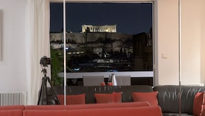 A modern living room with a large window overlooking a historic building. - Athens Urban Visions Art Apartment. Breath taking Views to Acropolis.  (Athina)