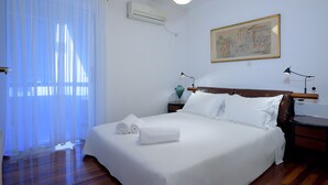 A neatly made bed with white linens, a wooden headboard, and a painting on the wall. - Athens Urban Visions Art Apartment. Breath taking Views to Acropolis.  (Athina)