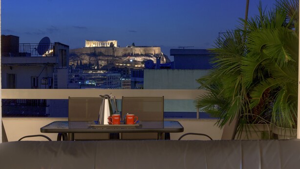 A balcony with a table and chairs, a potted plant, and a view of a historic building. - Athens Urban Visions Art Apartment. Breath taking Views to Acropolis.  (Athina)