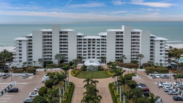 A multi-story hotel with a central courtyard, parking lot, and a view of the ocean. - Somerset 510- Beautiful Beach Front Condo! Lovely Beach Décor! (Marco Island)