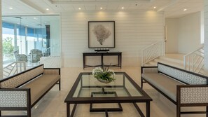 A modern lobby with a glass-top table, two sofas, a framed artwork, and a staircase. - Somerset 510- Beautiful Beach Front Condo! Lovely Beach Décor! (Marco Island)