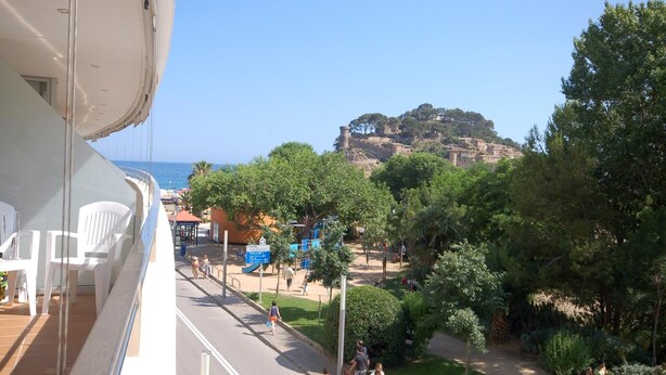 A balcony with white chairs, a view of a coastal town with a castle, and a playground area. - EXCELLENT APARTMENT NEXT BEACH (Tossa de Mar)